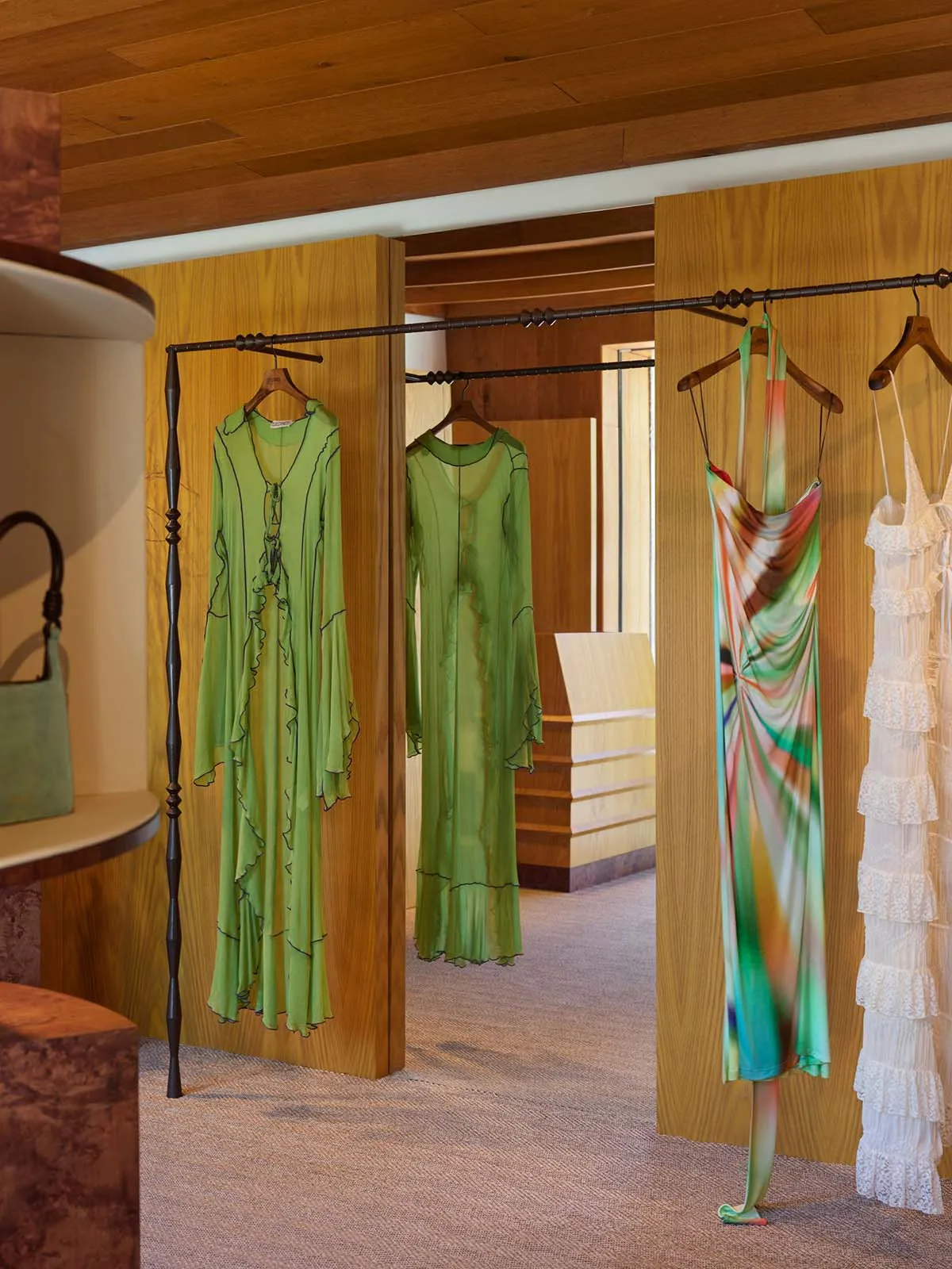 A clothing shop with dresses hanging on wooden hangers and a wooden ceiling.
