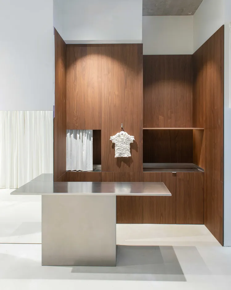 A modern retail shop displaying a white textured dress on a wooden background with a white curtain and a metallic table.