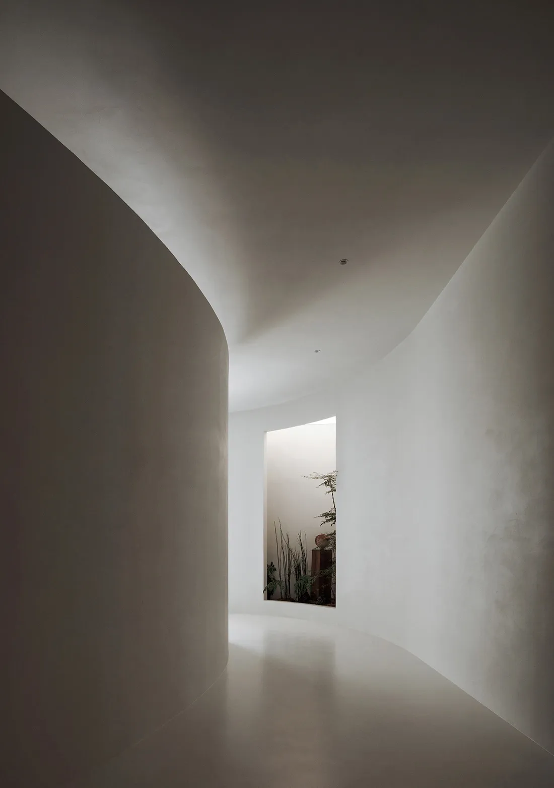 A minimalist hallway with curved concrete walls and a view of a serene garden
