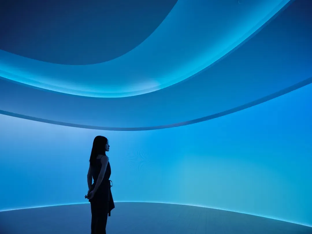A minimalist installation featuring modern lighting and digital projection in a large, open space.