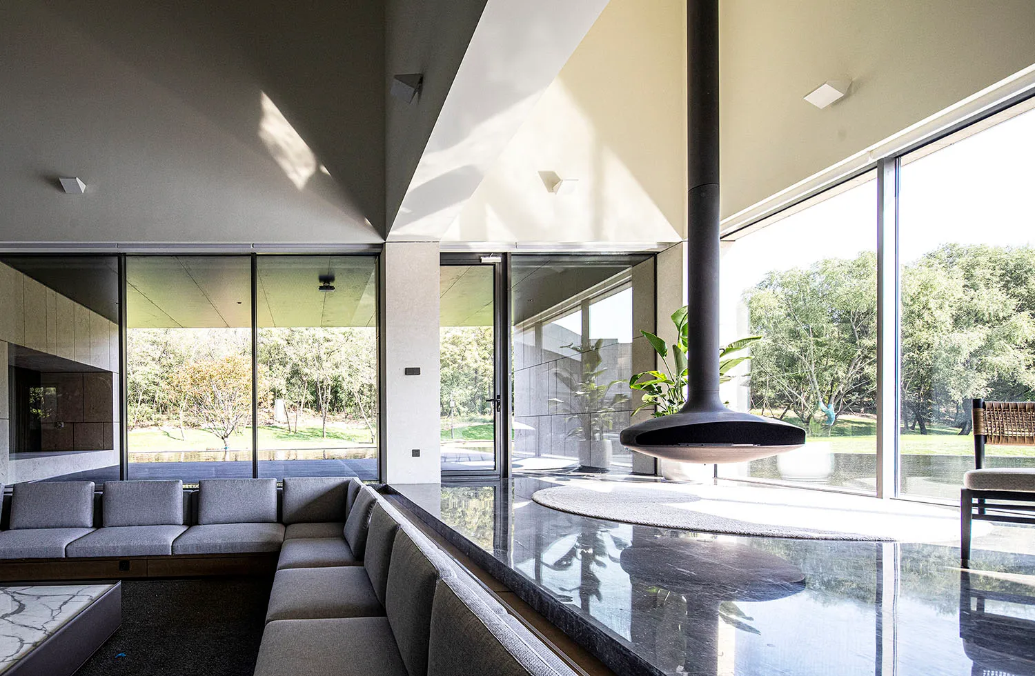 Modern living room with floor-to-ceiling glass windows, concrete walls, and a steel fireplace.