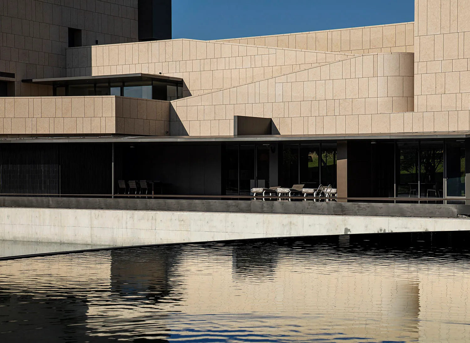 A modern public building with concrete and glass surfaces reflected in water.