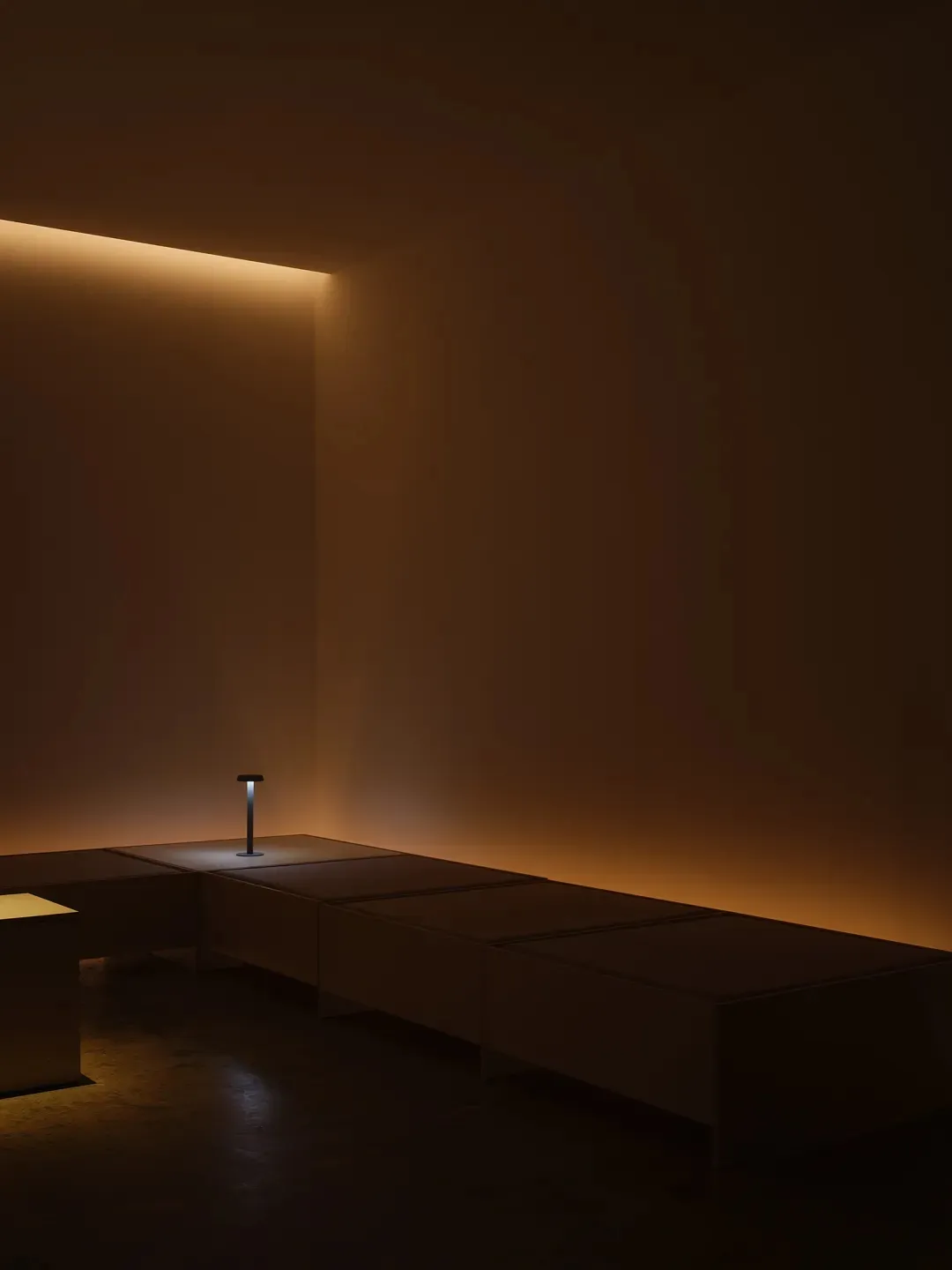 A minimalist interior space with a concrete bench and a small table lamp.