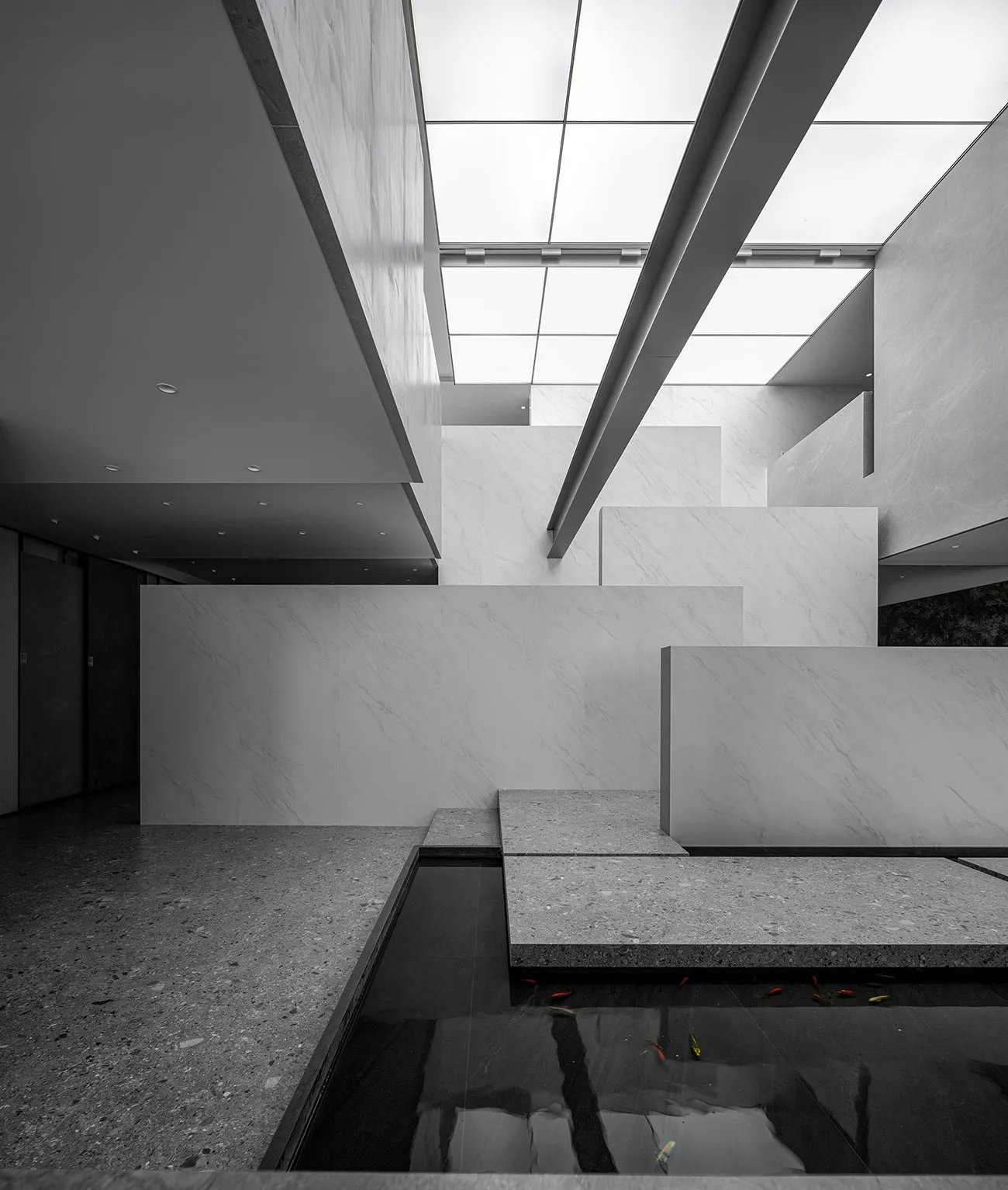 Modern interior design featuring a minimalist lobby with concrete and glass materials, illuminated by overhead lighting.