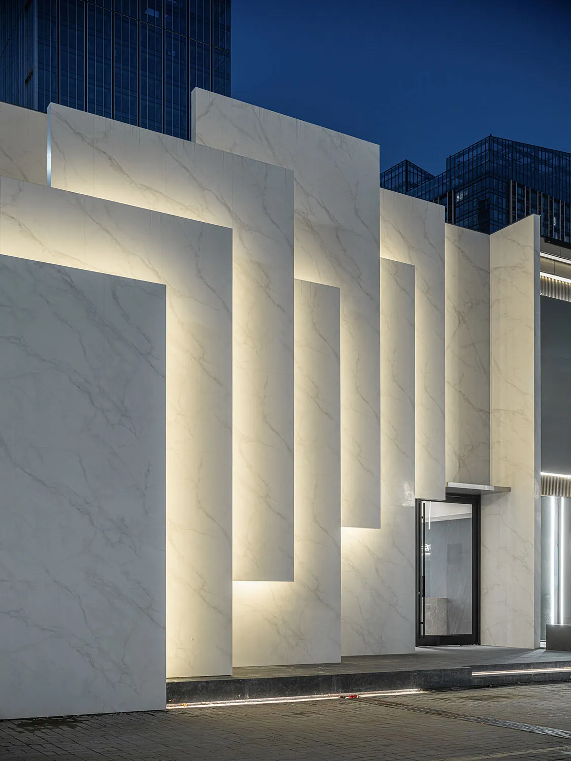 Modern storefront with illuminated marble columns at night.