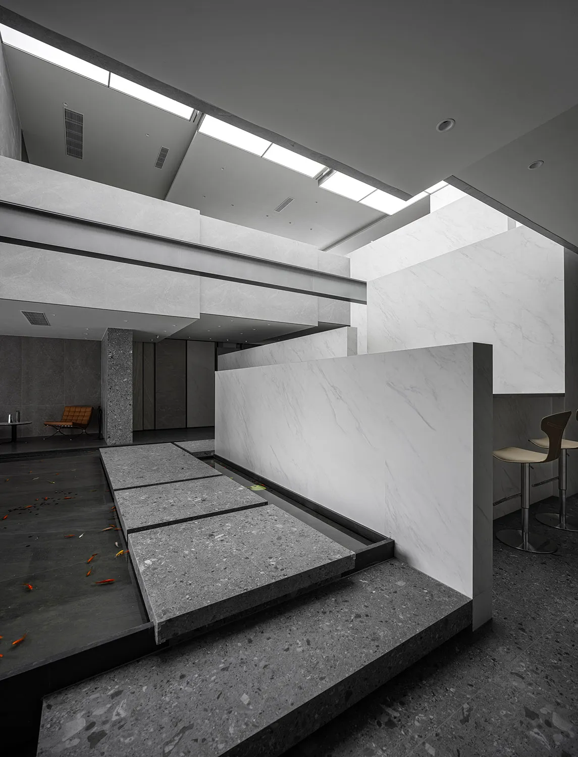 A modern lobby featuring marble and concrete walls, with a water feature and seating areas.