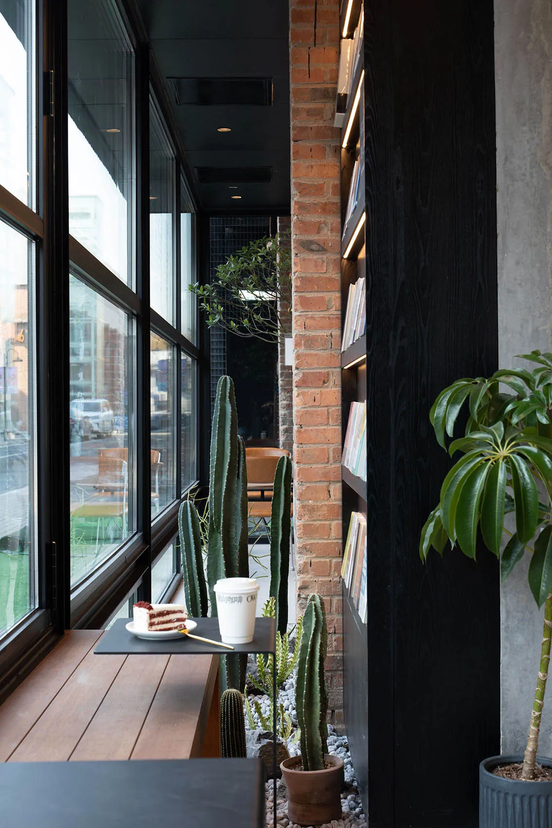 Café interior with a brick wall, concrete columns, and greenery.