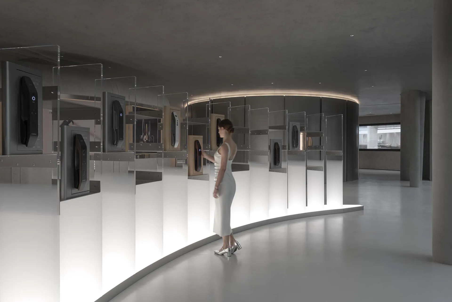 A woman in a white dress examines clear glass cases in an exhibition space.