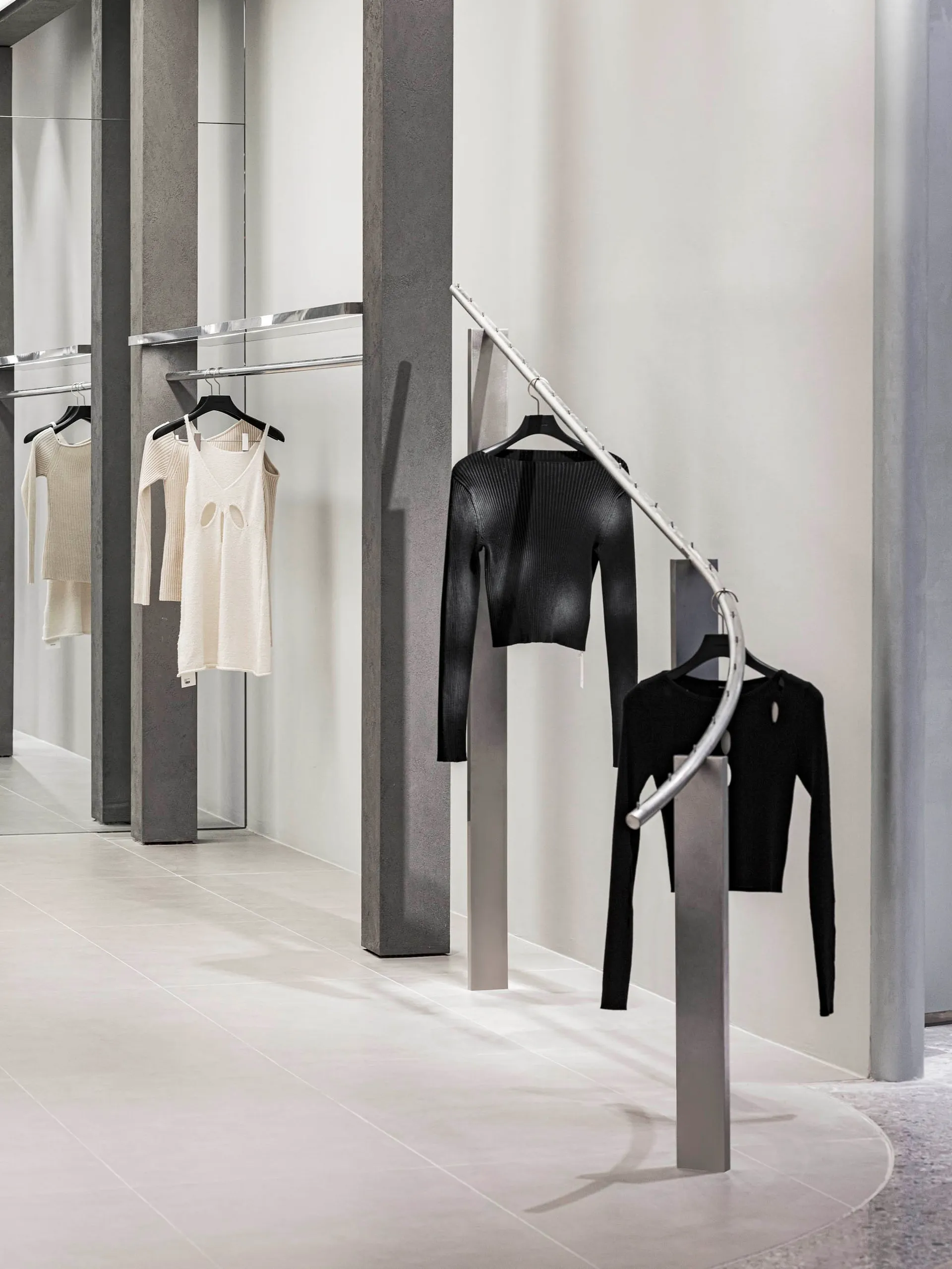 A modern retail clothing store displays minimalist clothing on metal hangers with a concrete and glass interior design.
