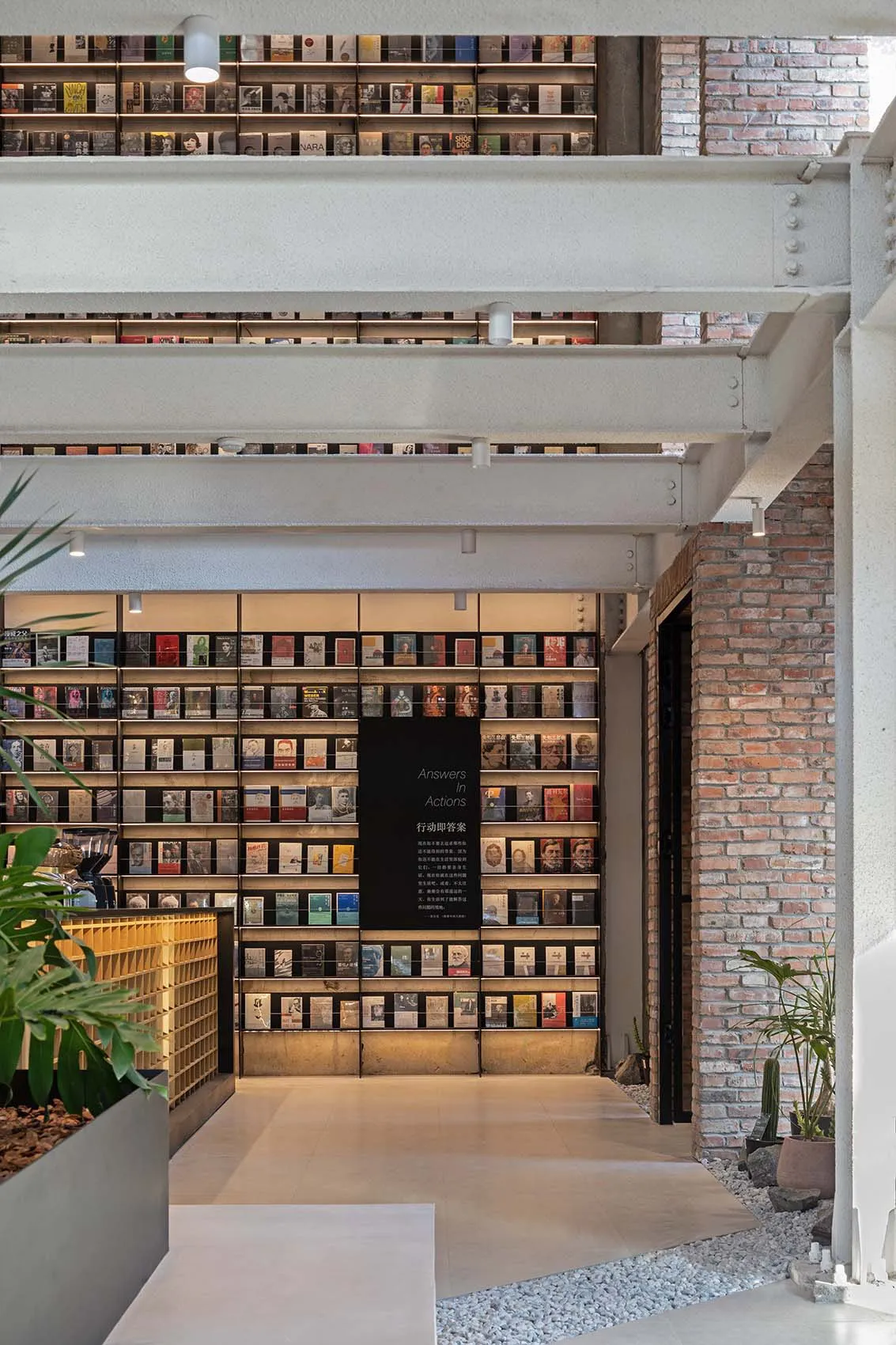 A modern library with exposed brick walls and concrete flooring, featuring metal shelving units filled with books and a centr
