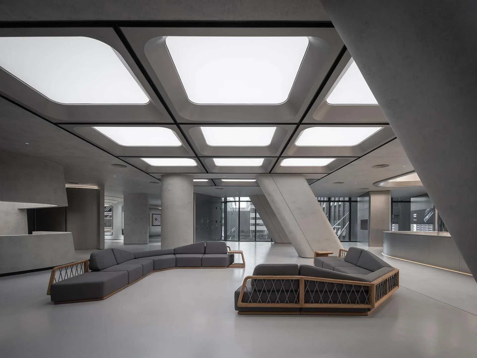 Modern minimalist office lobby with concrete walls and floors, featuring sleek furniture and large skylights.