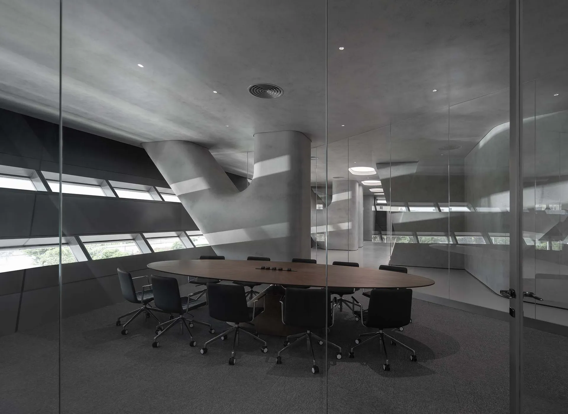 A minimalist conference room with concrete walls and a large oval table surrounded by black chairs.