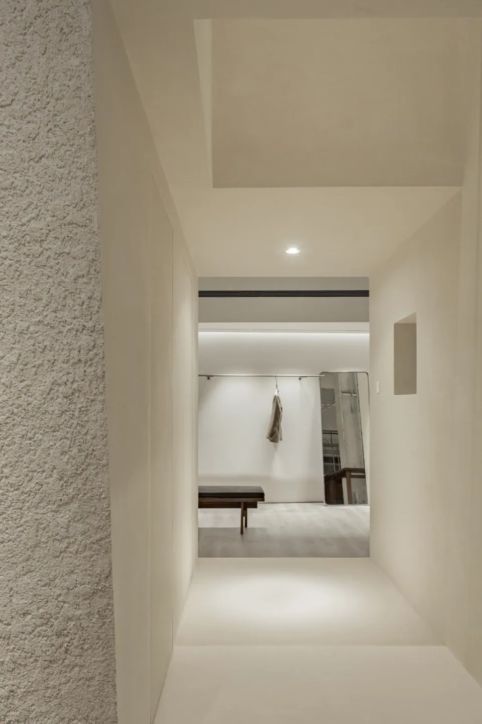 A minimalist room with concrete walls and floor, minimal furniture, and a single jacket hanging on the wall.