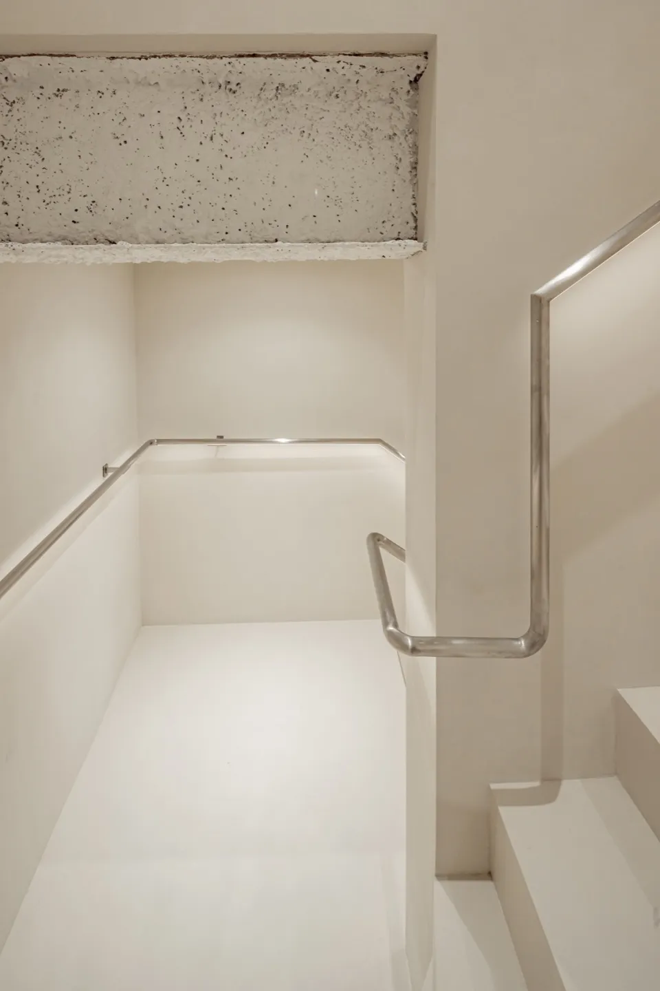 A minimalist stairwell with concrete flooring and stainless steel railings.