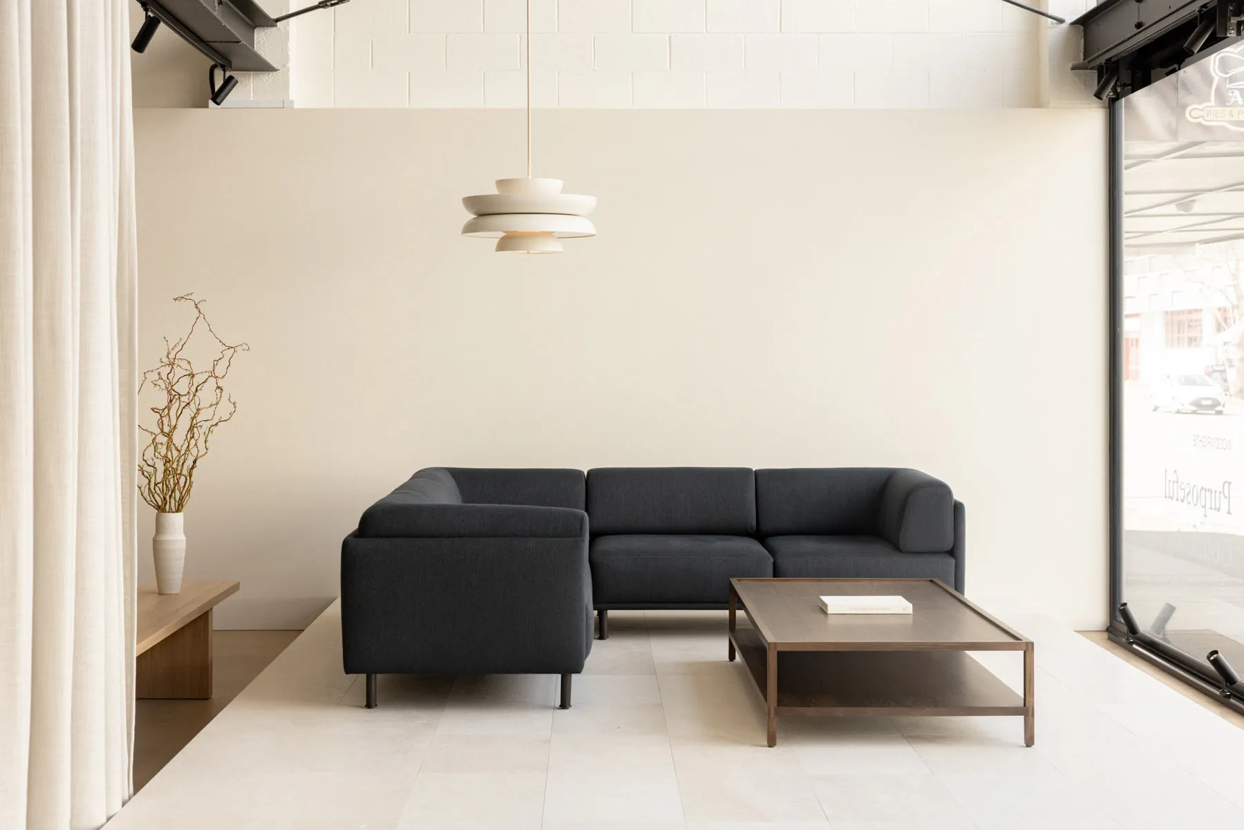 Contemporary living room with a black sectional sofa and a white pendant light hanging above, against a white wall.