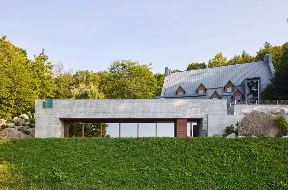 A modern residential house with a concrete exterior and a green hedge in the foreground.