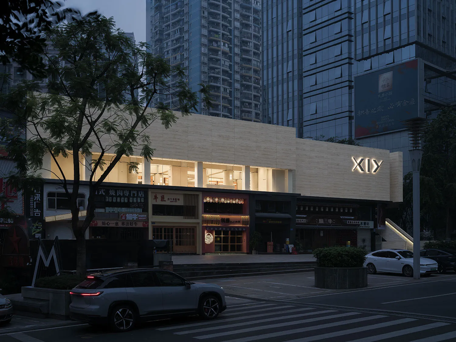 Modern retail storefront with concrete exterior, illuminated signage, and vehicles parked in front.