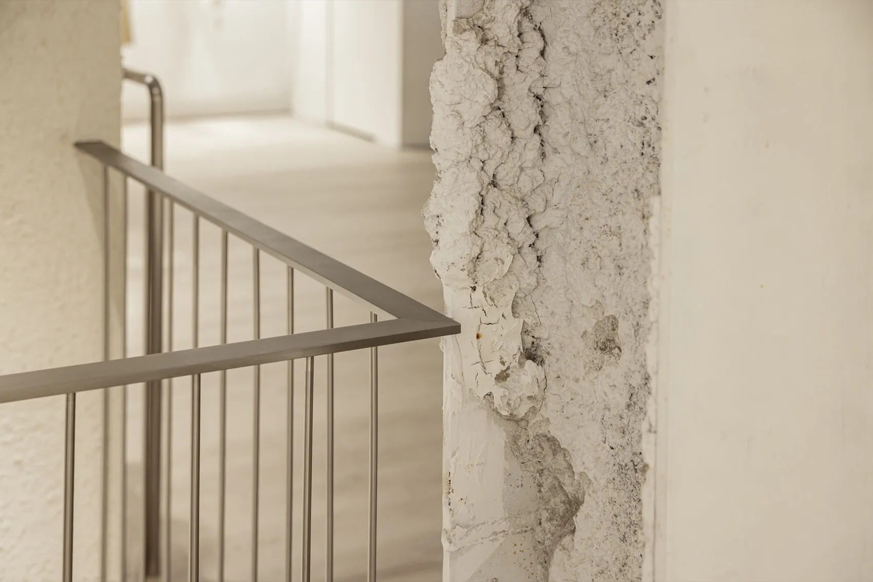 A close-up view of a stairway with a concrete wall featuring a textured, cracked surface and a metal railing.