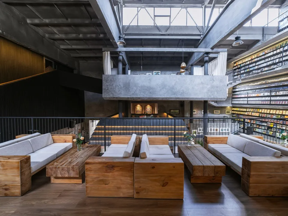 A modern industrial library restaurant featuring exposed concrete ceilings, wooden furniture, and a spacious, open design.