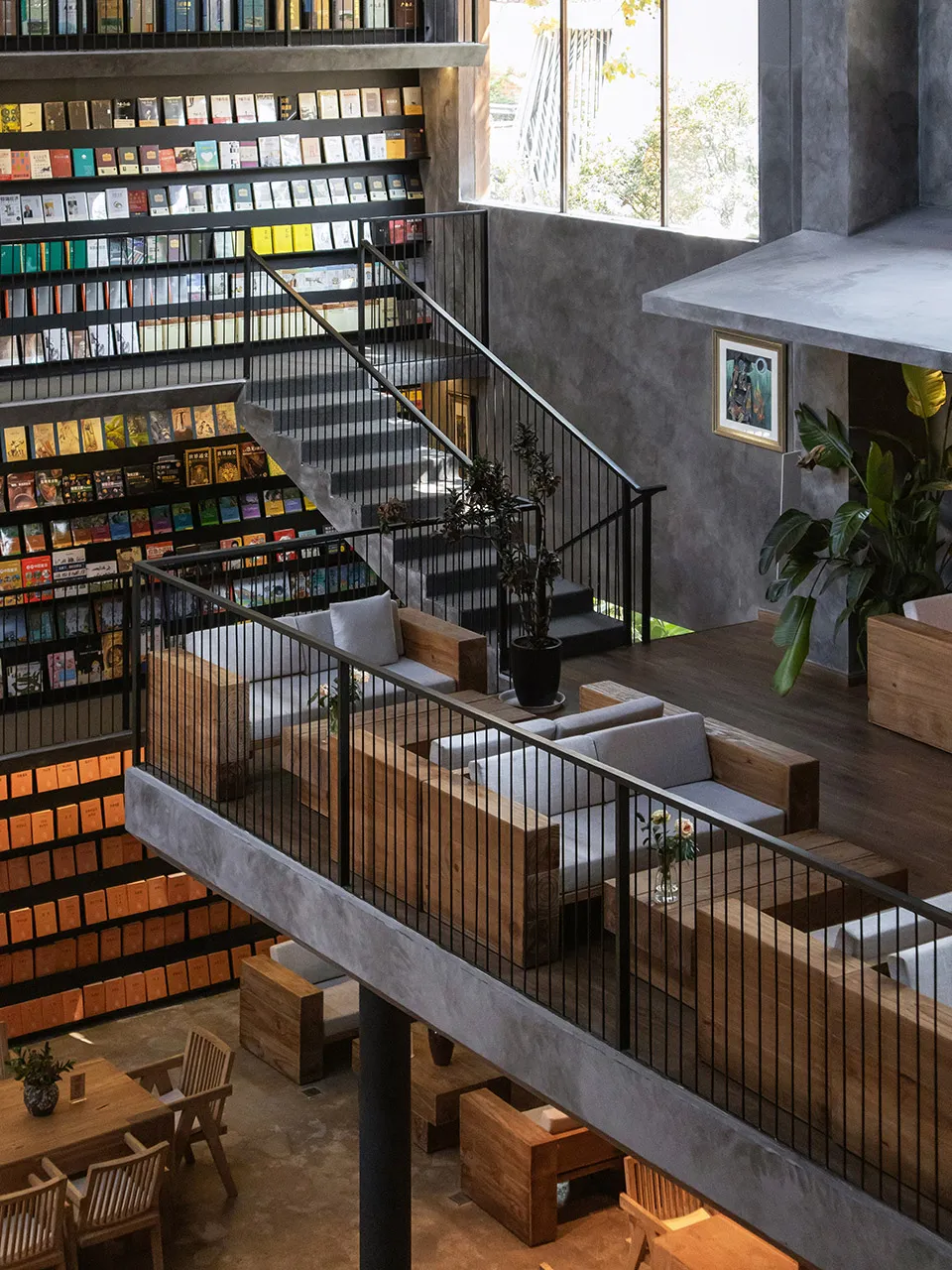 A modern industrial library and child's playroom with concrete and wood materials, featuring seating and bookshelves.