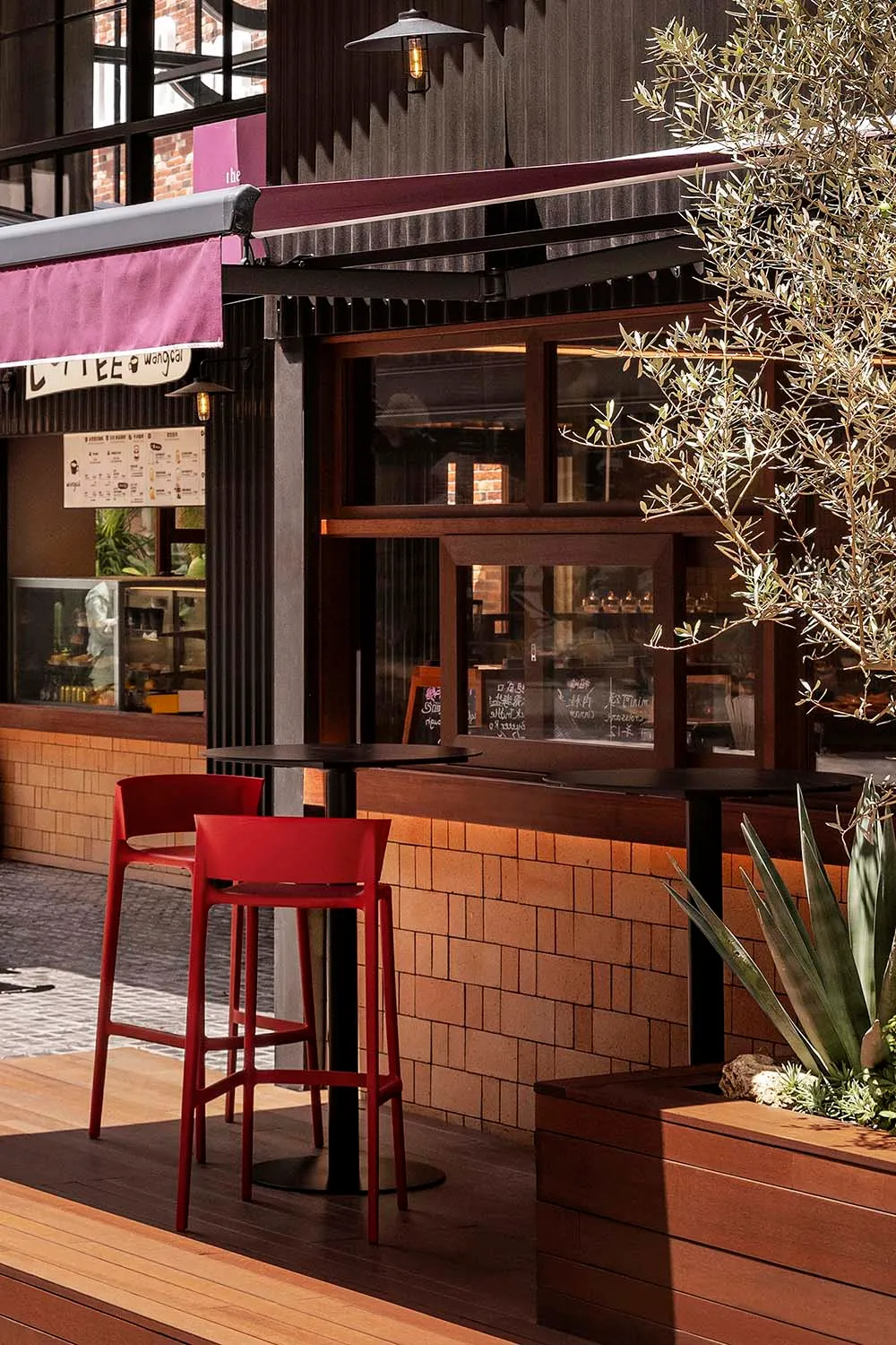 An industrial-style cafe interior with wood accents, high stools, and potted plants.