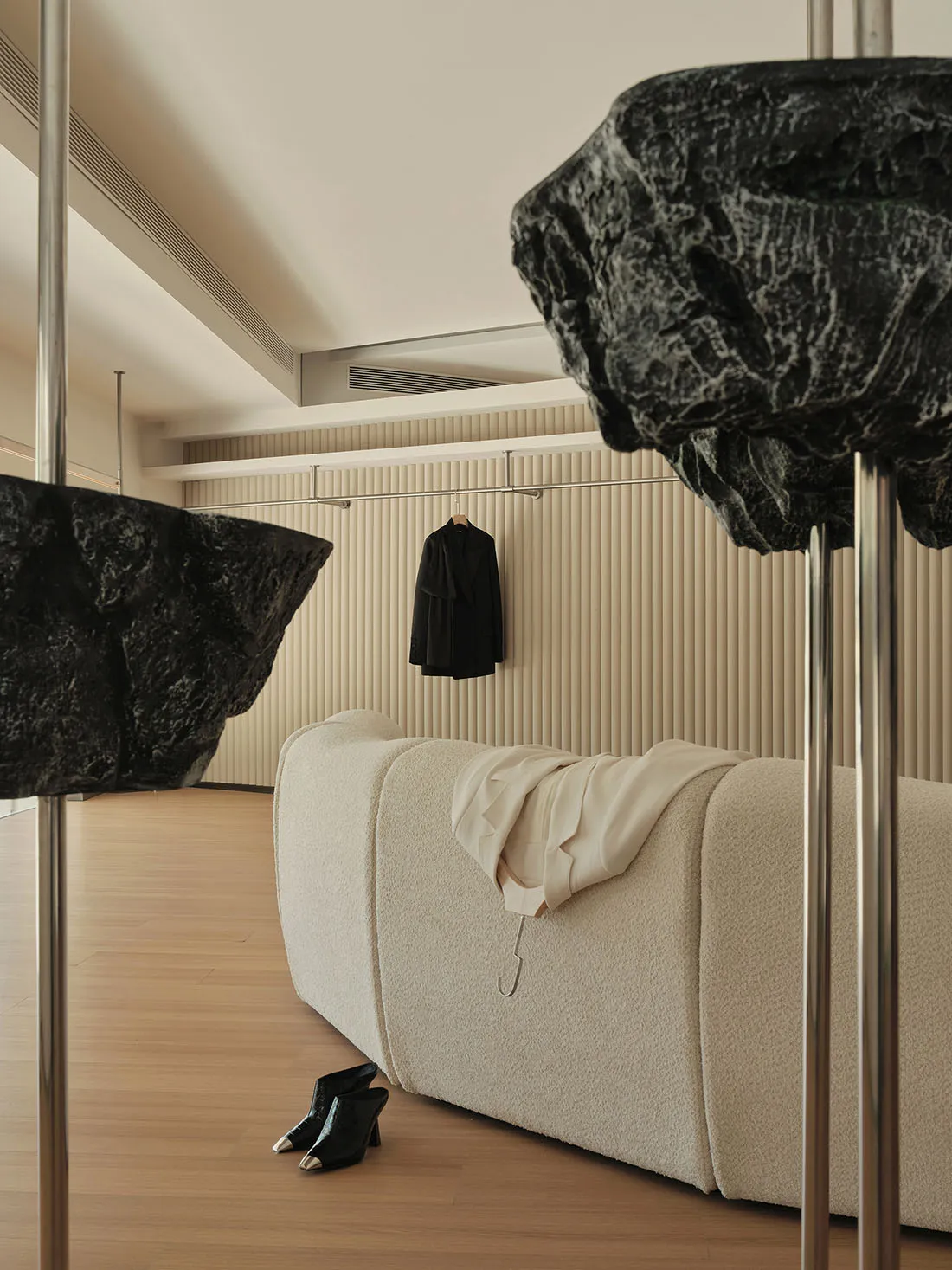 A minimalist living room with a sofa, black jacket hanging on the wall, and black shoes on the floor.