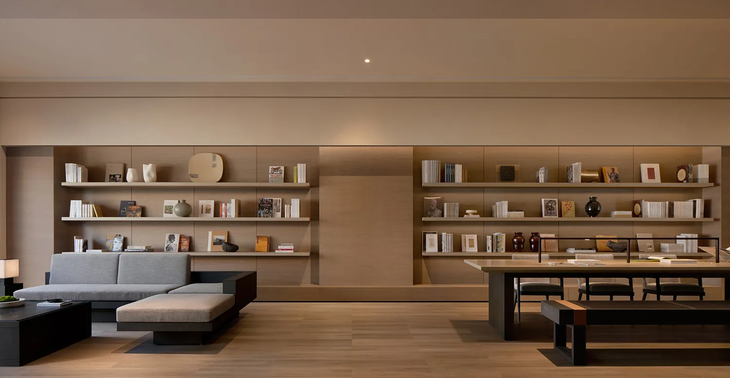 A modern library with wooden shelves containing books and decorative items. The floor is wooden, and there is a large sofa in