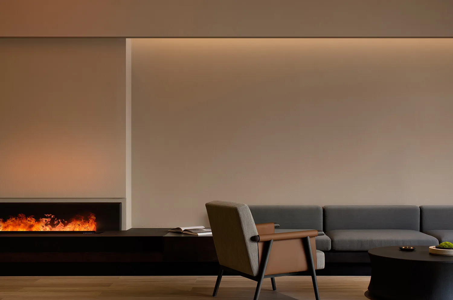 Modern living room with minimalist furniture, a grey sectional sofa, a brown armchair, and a fireplace with a warm ambient li
