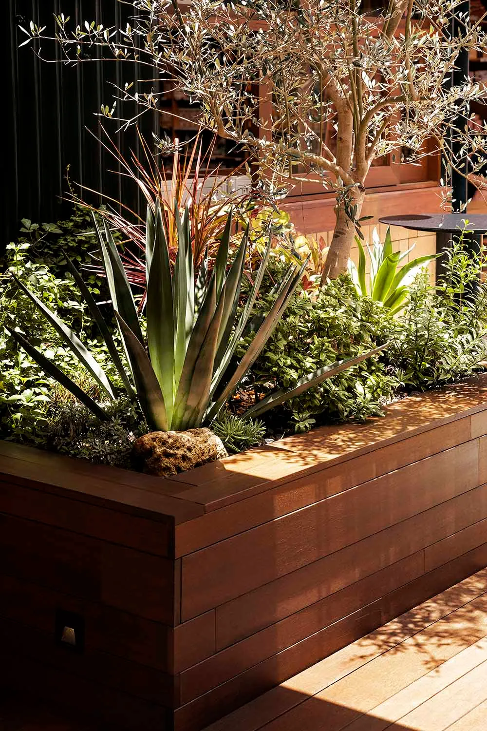 A modern plant display featuring a wooden planter with various plants and a rock element.