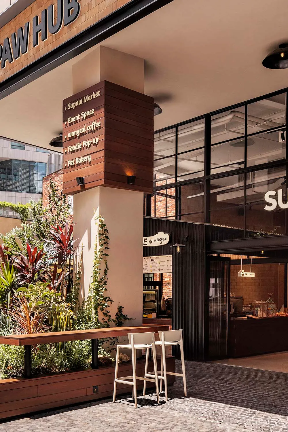 Concrete and glass exterior of a coffee shop with greenery and seating.