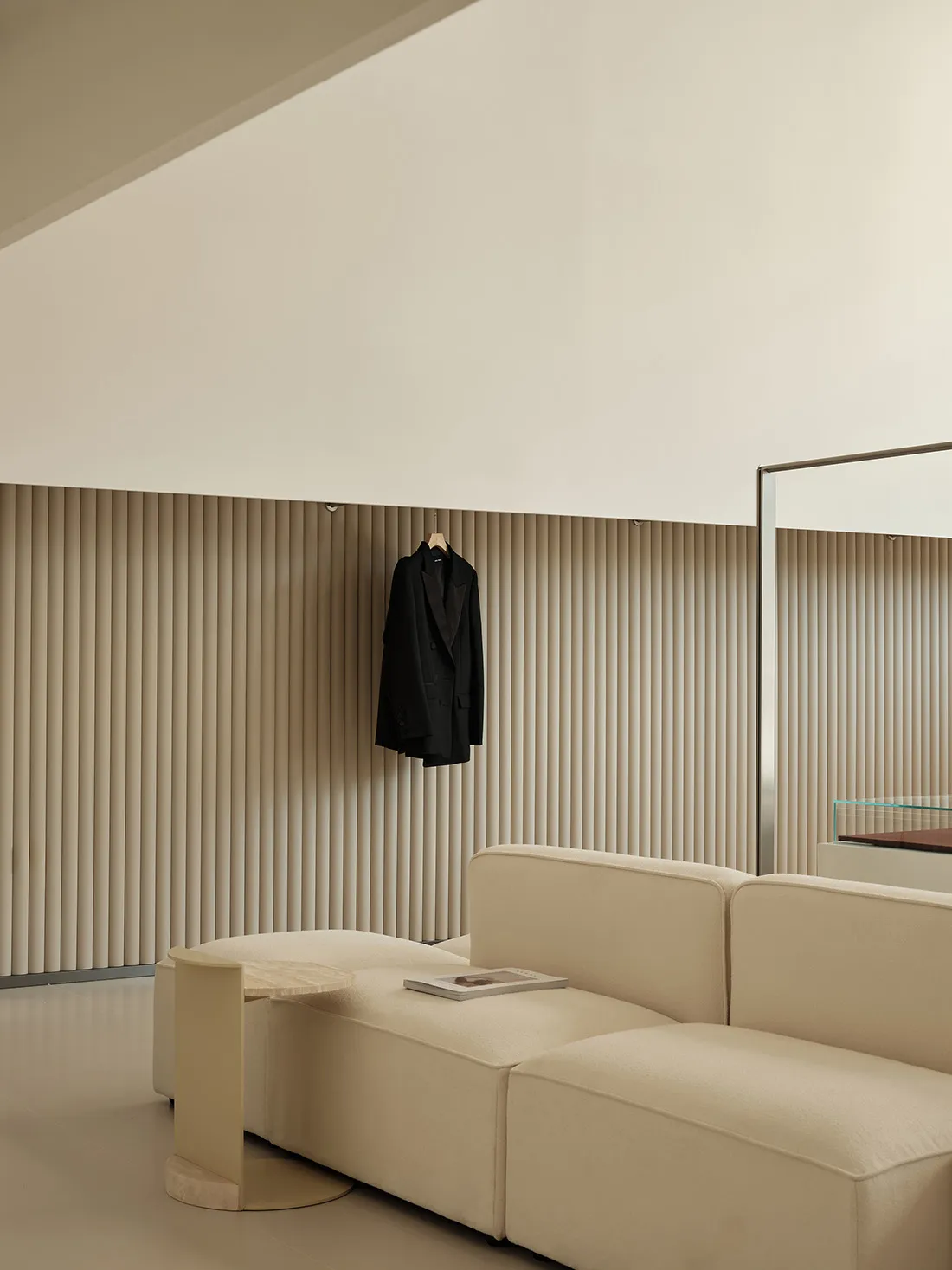 Minimalist living room featuring a beige sofa, plush cushions, vertical blinds, and a sleek mirror.
