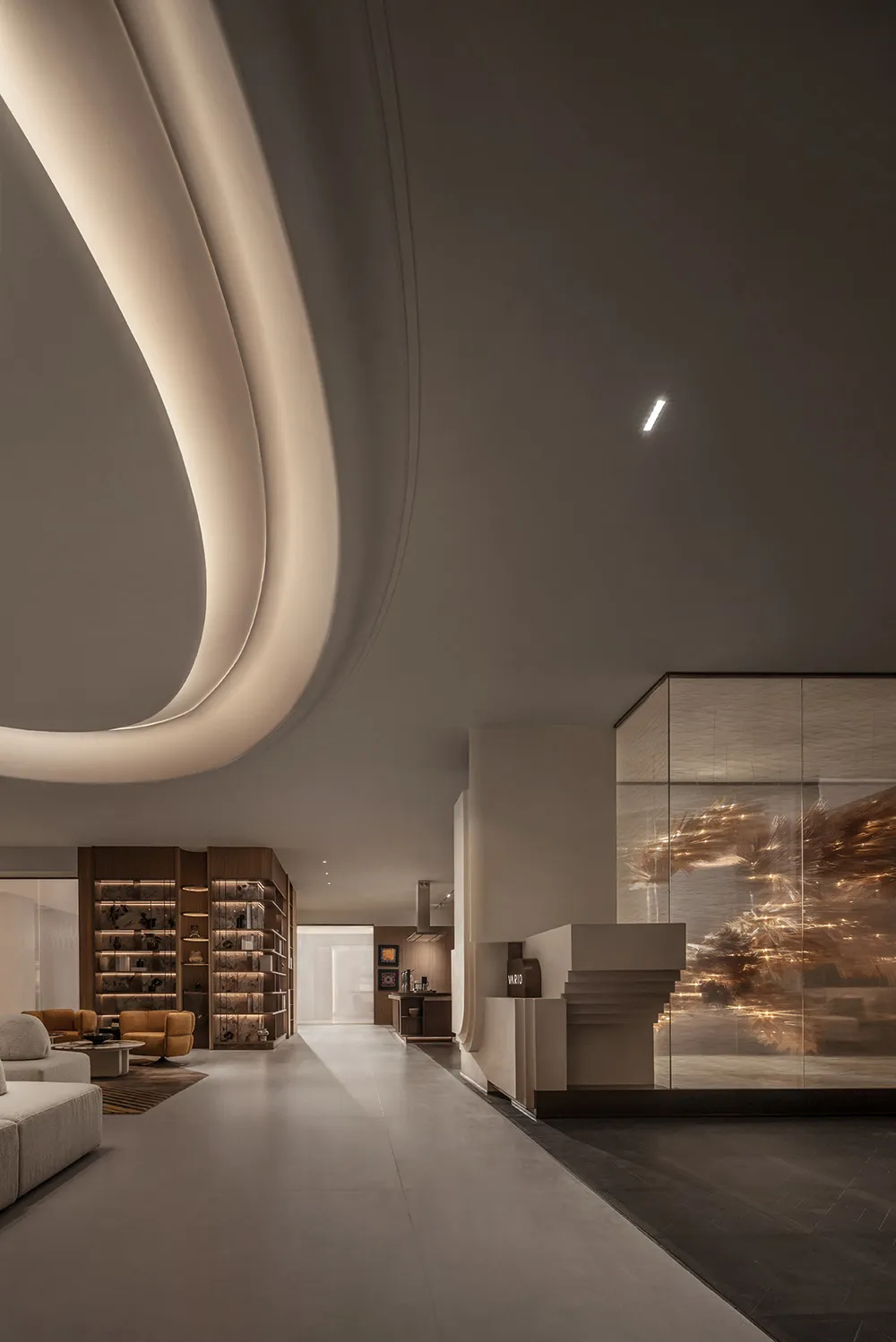 A modern lobby with concrete walls and floors, featuring curved ceiling lights and a glass wall with textured glass.
