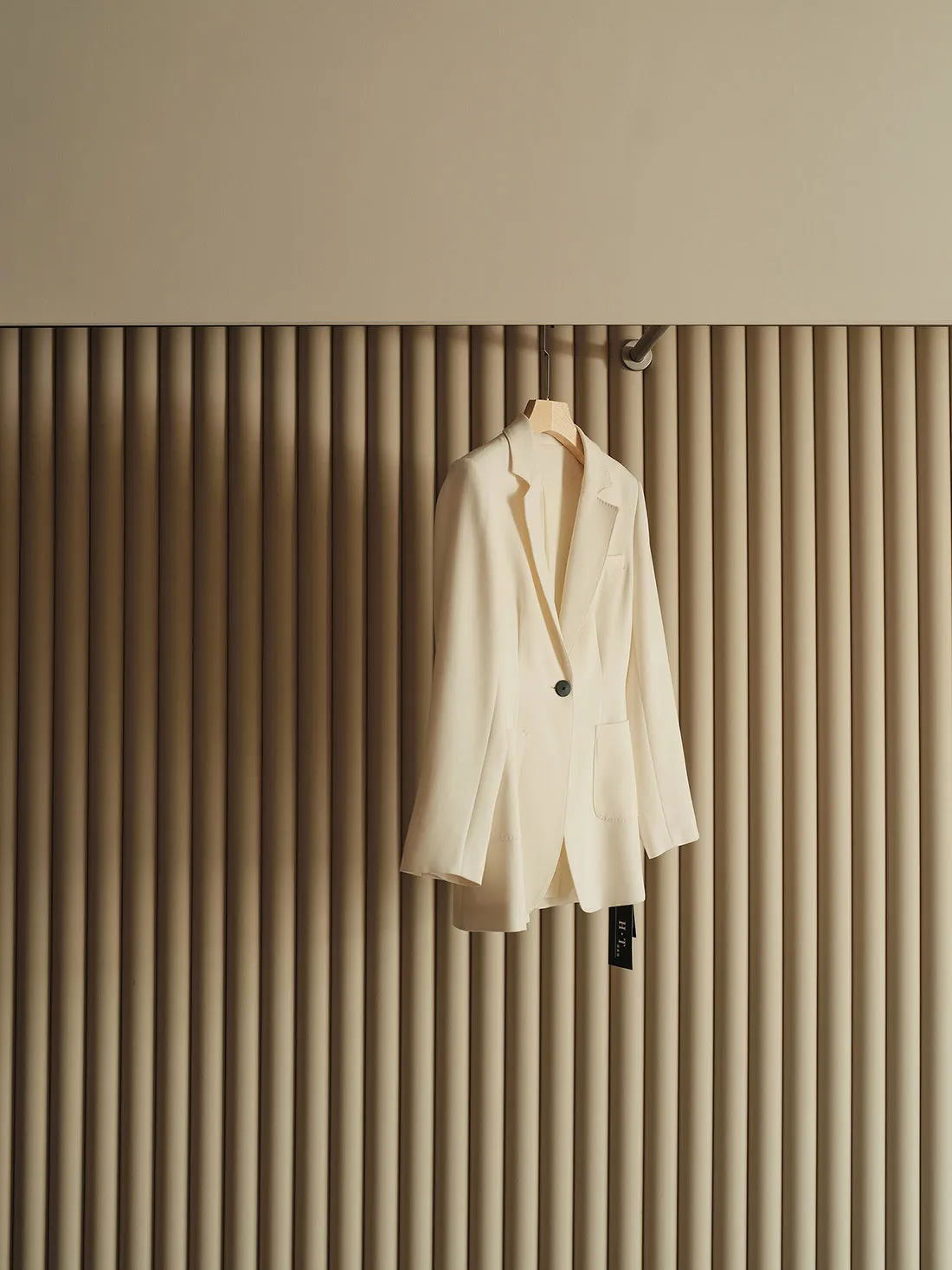 A white blazer hanging on a set of vertical beige curtains.