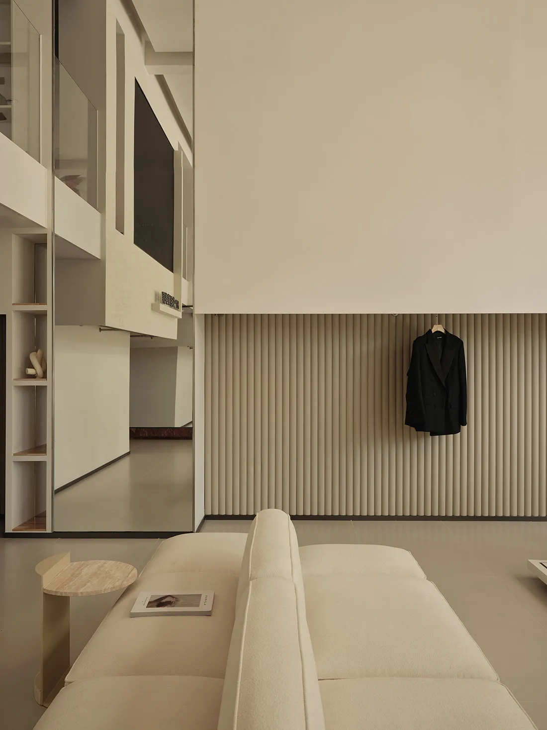 A minimalist living room with neutral-toned furniture and a black blazer hanging on the wall.