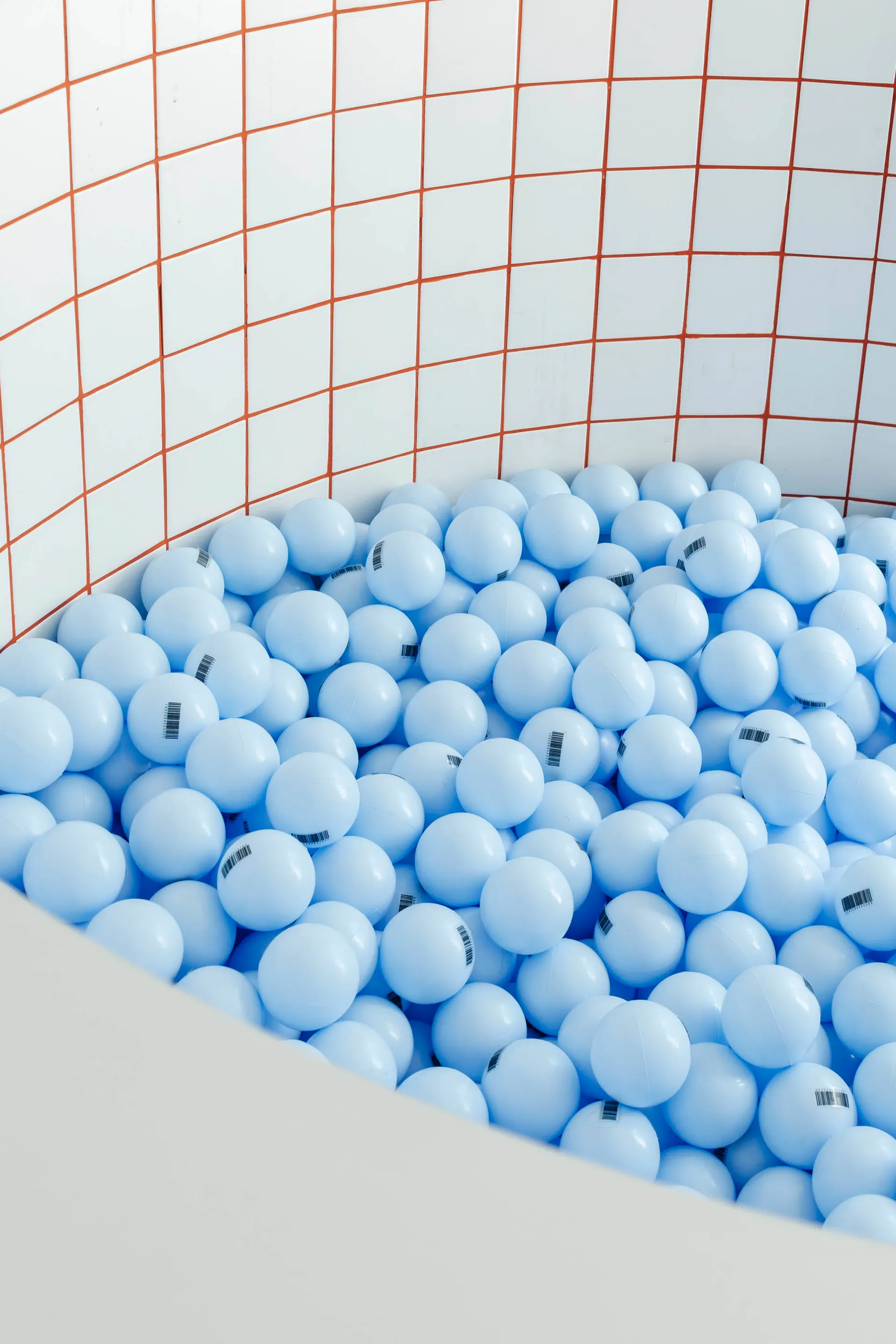 A minimalist playroom filled with blue plastic balls on a white tiled floor.
