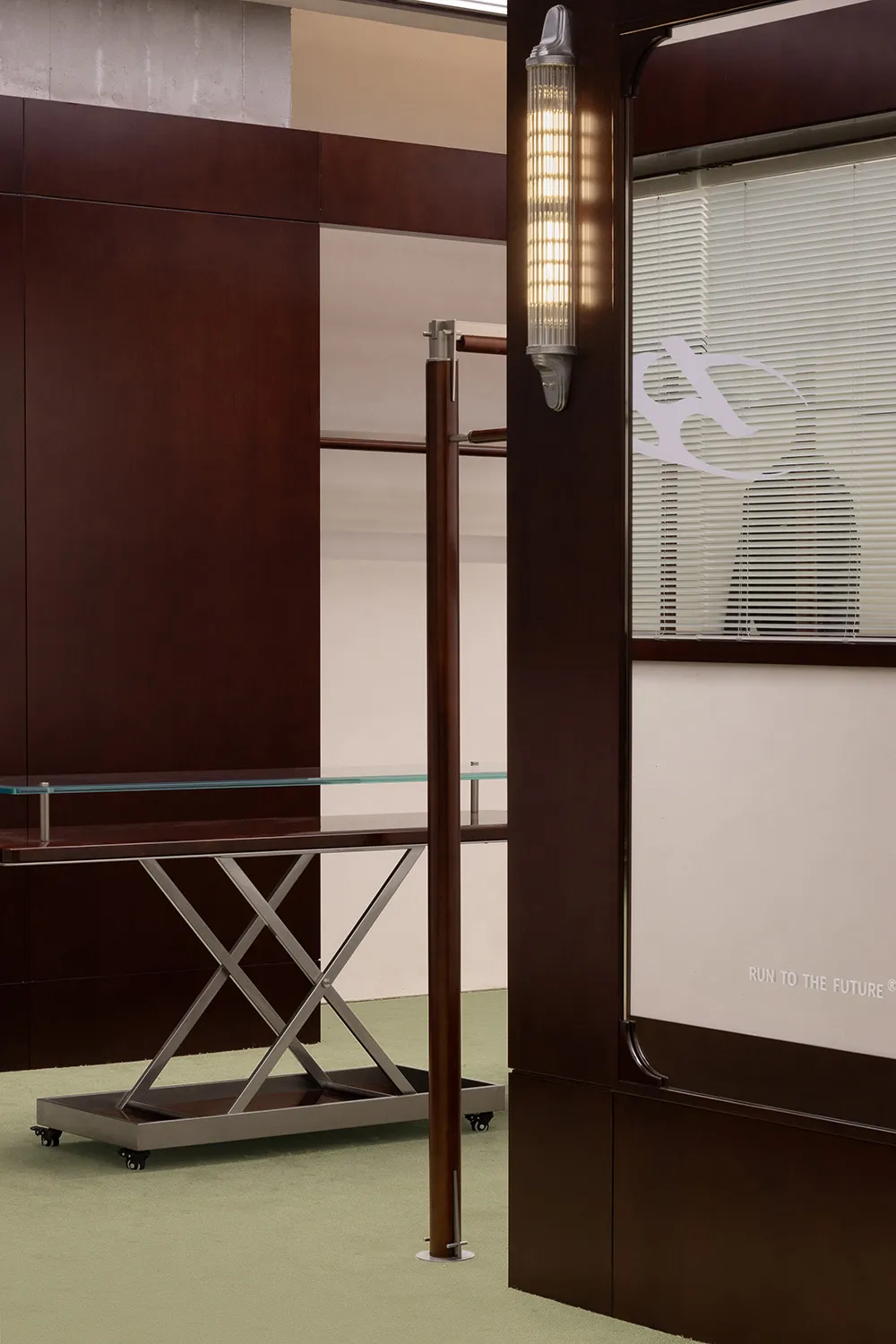 A minimalist interior design featuring a modern metal shelf with a glass top on a green carpeted floor.
