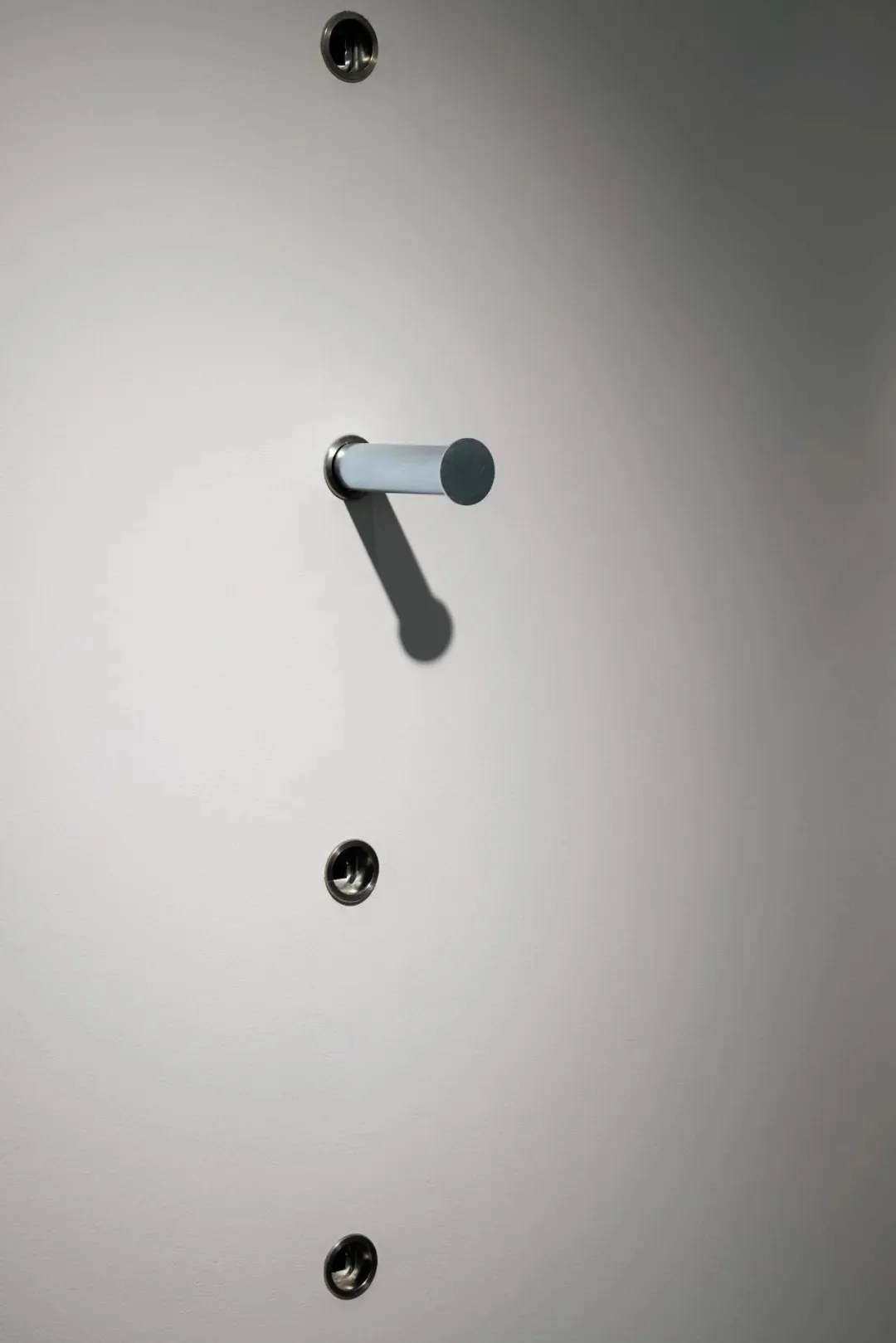 A metal lock with a gray cylinder handle attached to a smooth, white surface.