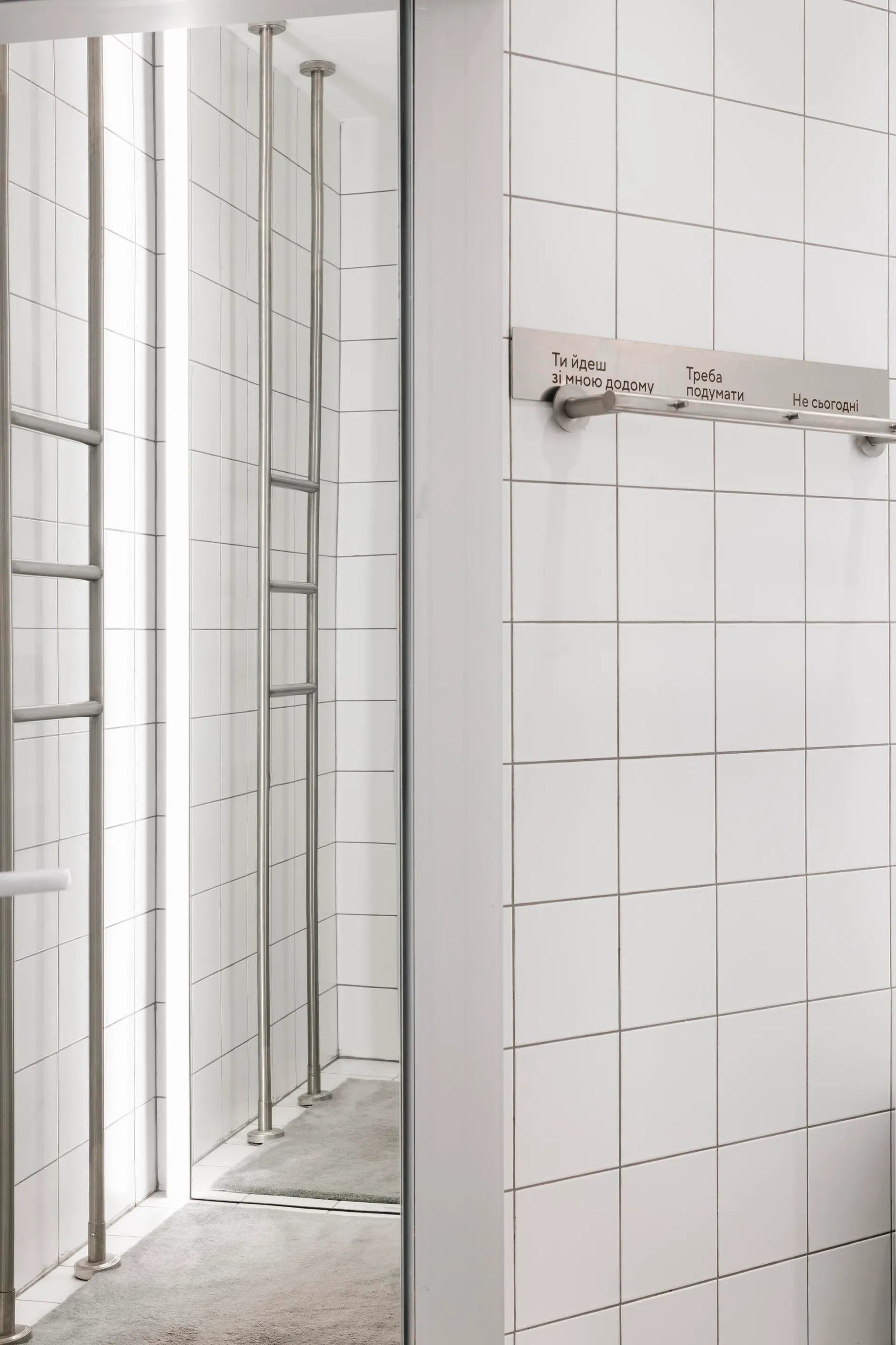 A modern public space with white tiled walls and arms attached horizontally with writing