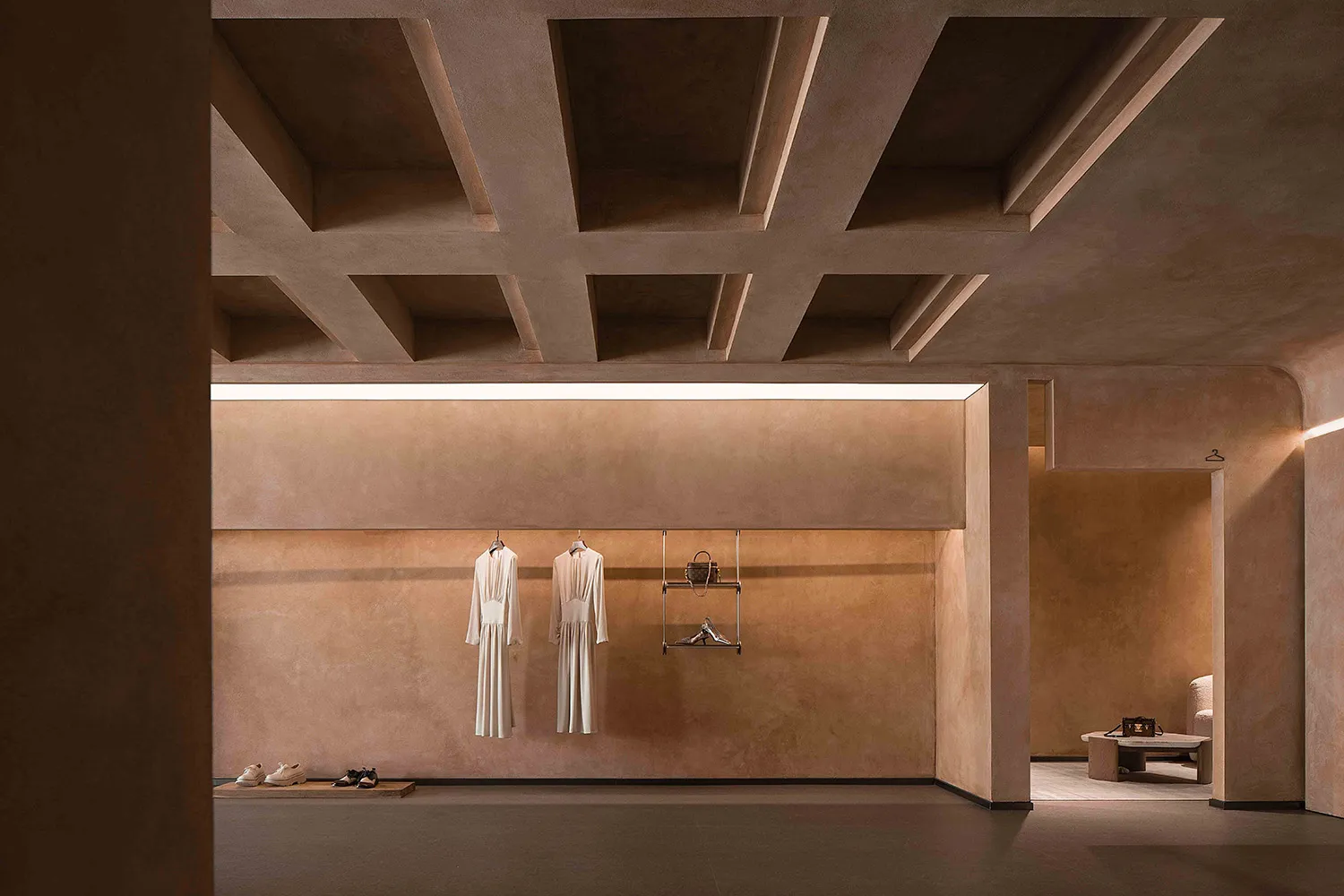 A minimalist retail store with a terracotta-colored wall and white dress hanging on a clothes hanger.