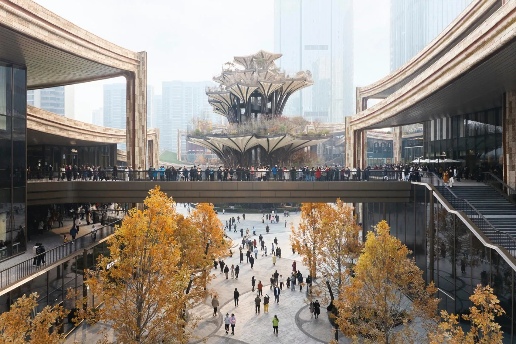 A modern public square featuring concrete and glass structures, with people gathered in the open space.