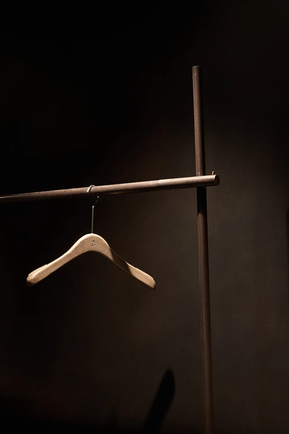 A minimalist wooden clothing hanger suspended from a dark metal rod.
