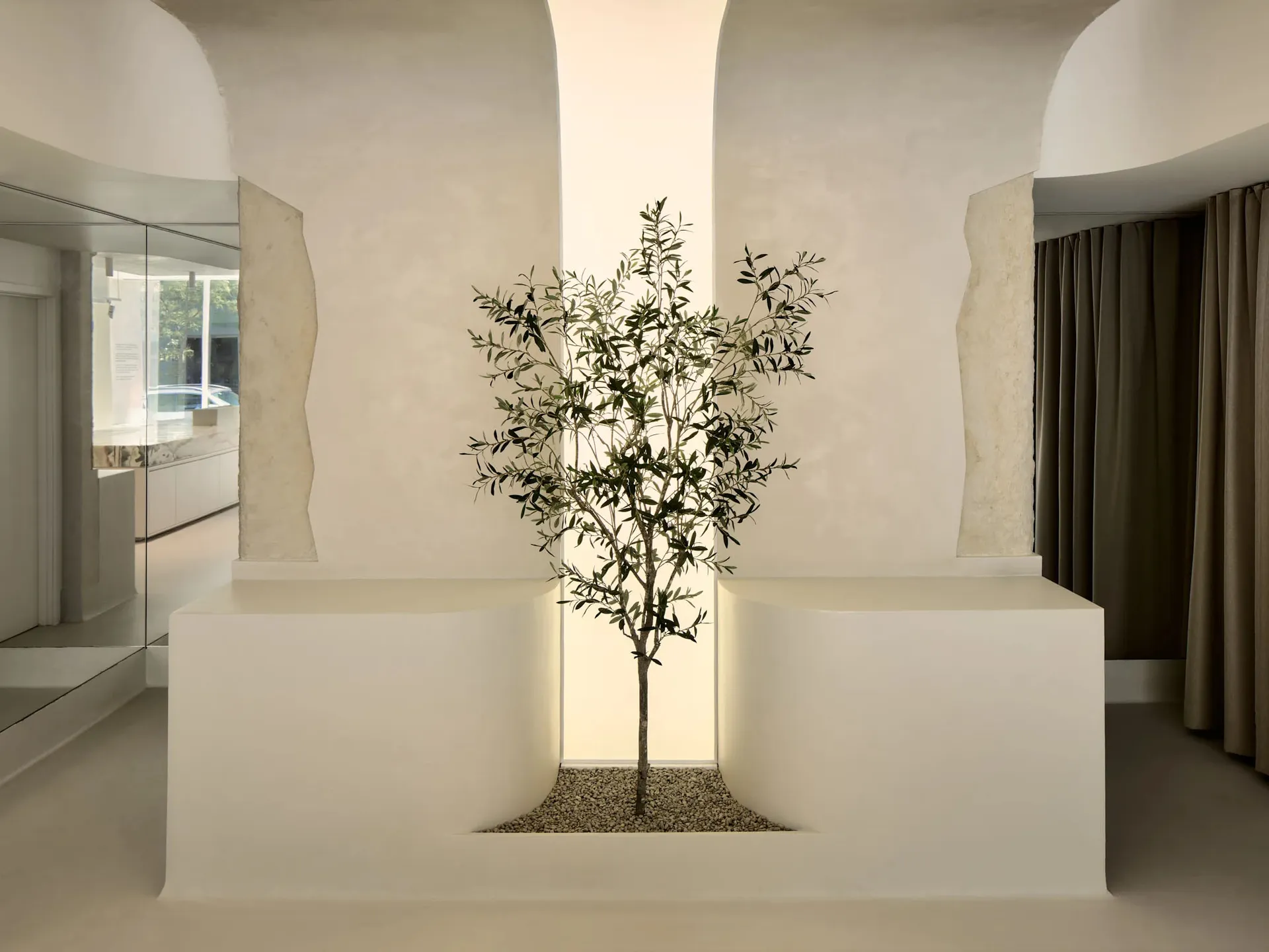A minimalist interior space featuring a concrete tree planted in a square, illuminated niche.