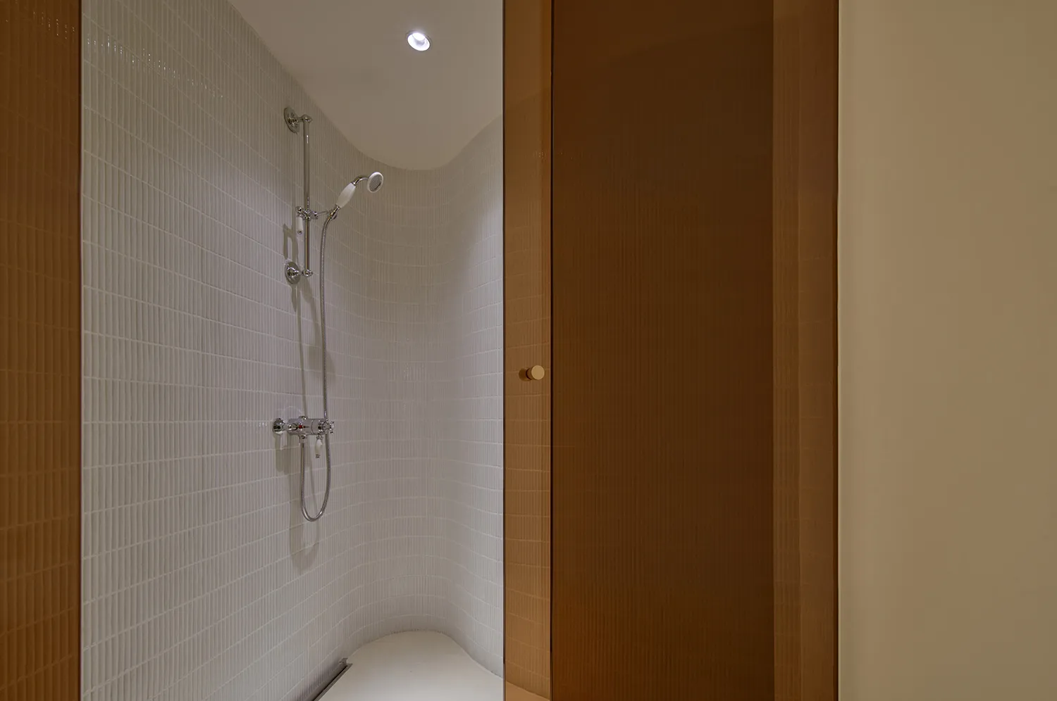 Minimalist bathroom with white tiled walls and floor, featuring a walk-in shower.