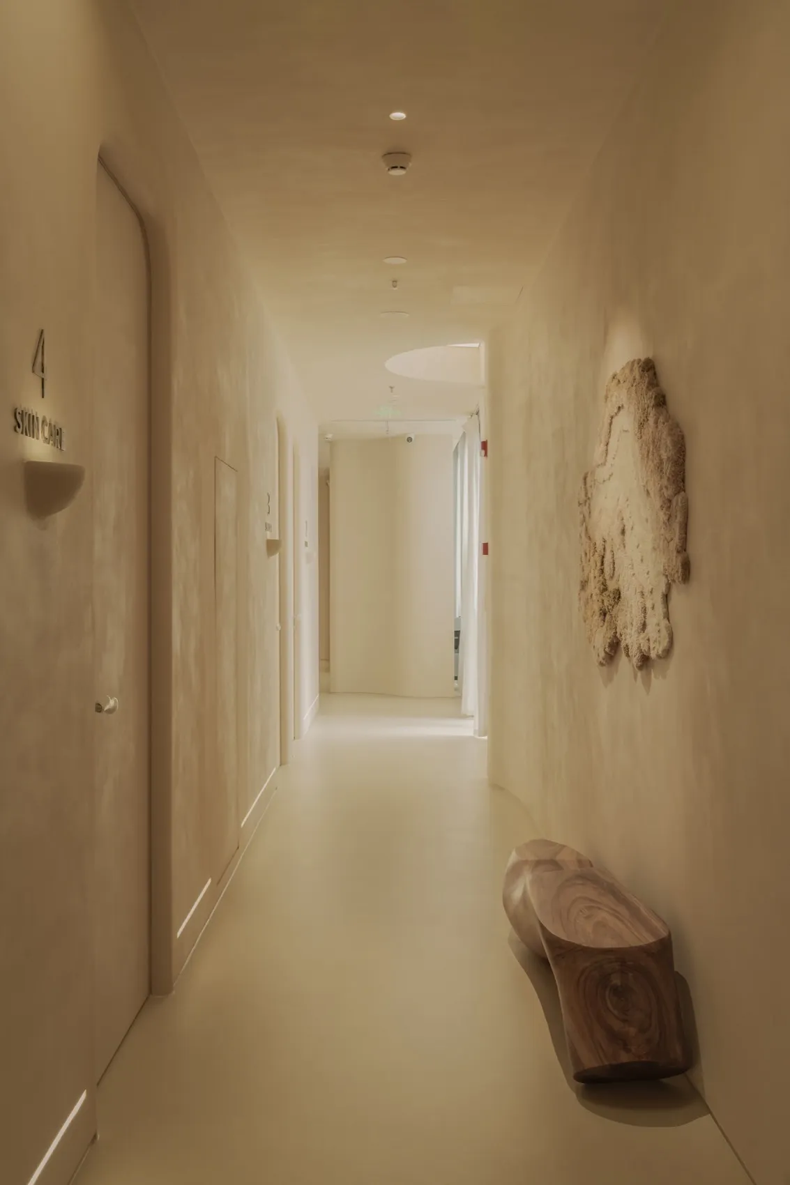 Modern minimalist corridor with concrete walls and floor, featuring a wooden bench and a textured wall hanging.