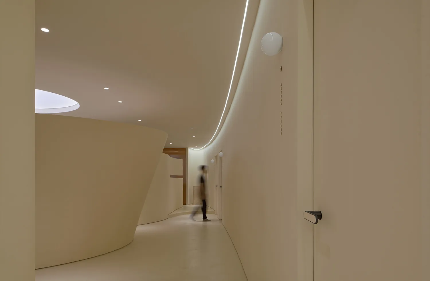 A modern office hallway with minimalistic design, white concrete walls, and a single person walking.