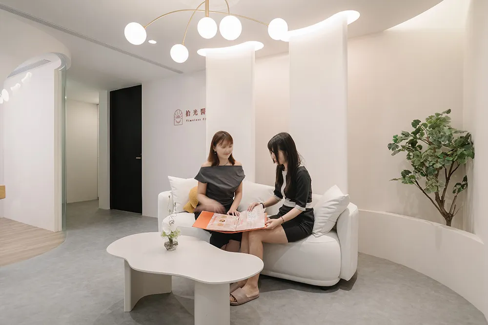 Two women sitting on a white sofa in a minimalist office setting.