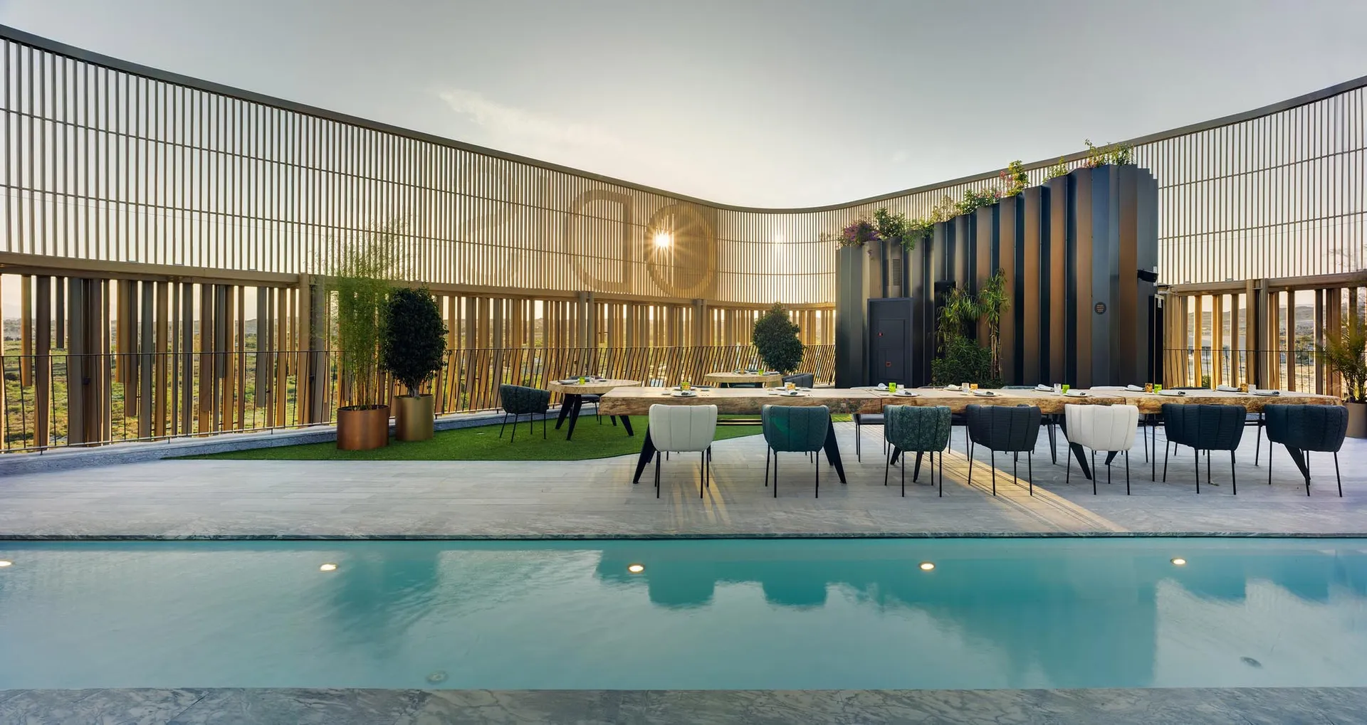 Modern outdoor dining area featuring wood and greenery with a swimming pool.