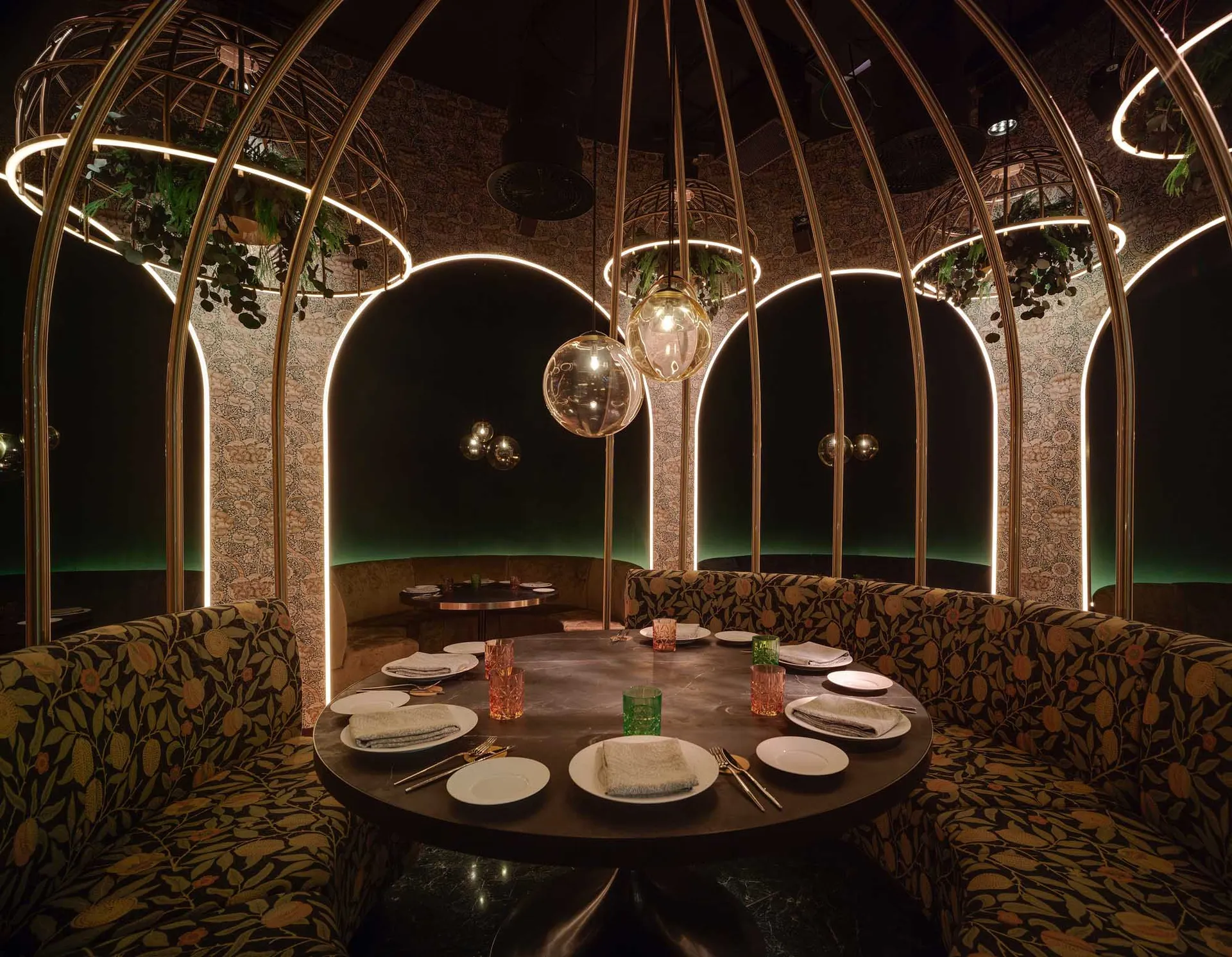 A round dining table surrounded by booth seating in a modern restaurant interior with metal arches and textile upholstery.