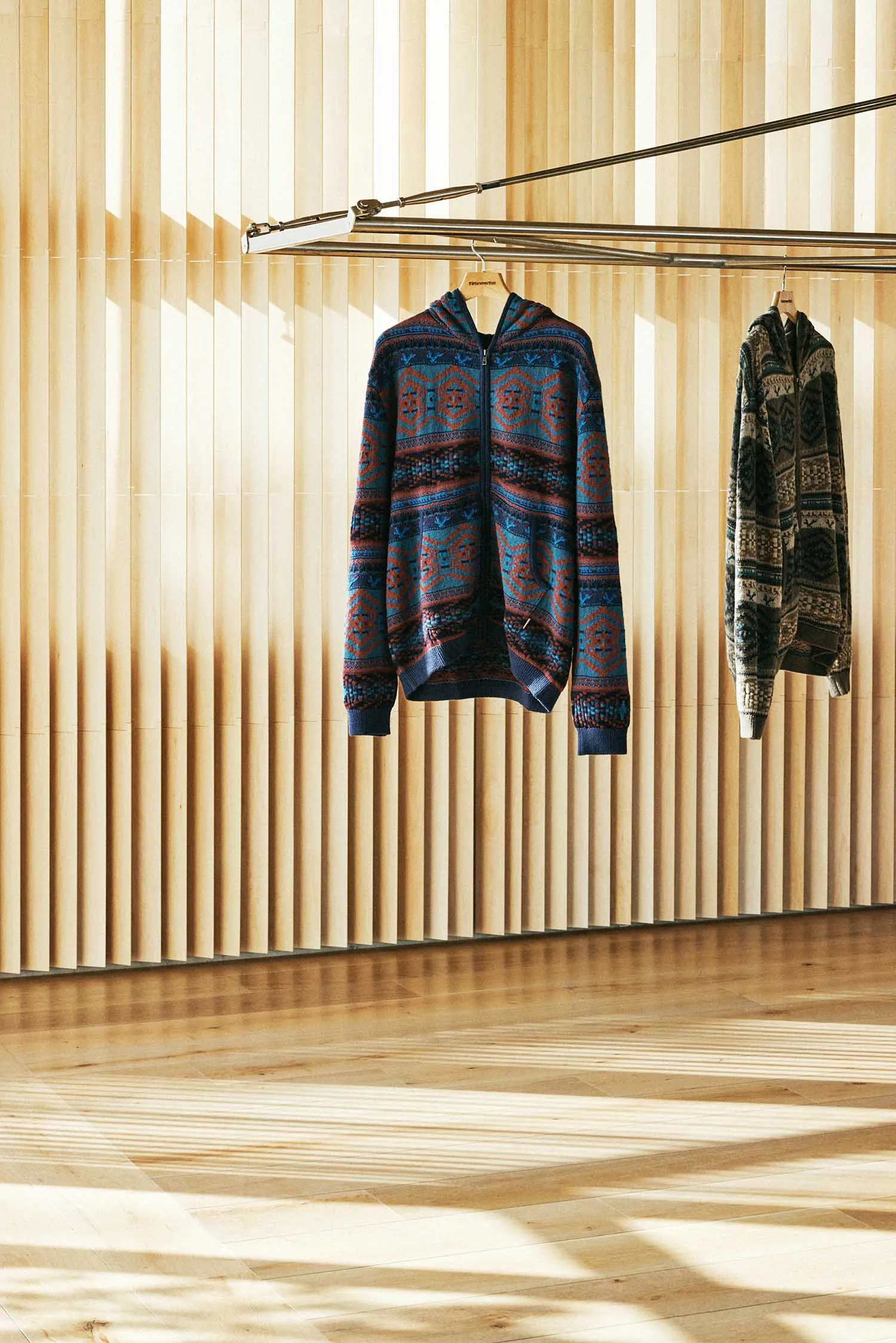 A clothing display featuring a sweater with a blue and brown geometric pattern hanging on a wooden wall.