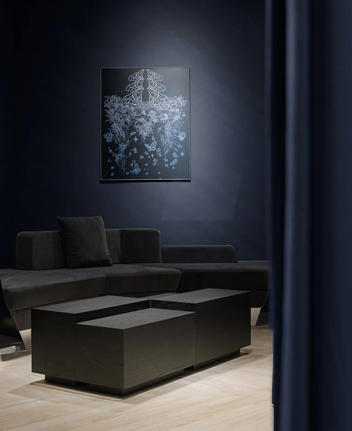 Modern living room featuring a dark grey sofa, a wooden coffee table, and a framed artwork on the dark blue wall.